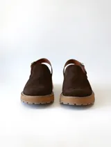 Zueco de cuero gamuzado color chocolate, con diseño de punta cerrada y tira ajustable con hebilla metálica en el talón. Presenta una suela de plataforma dentada en tono marrón claro.