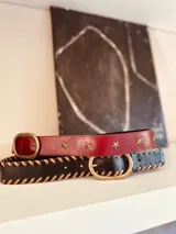 Cinturón de cuero negro con costuras decorativas color camel y hebilla ovalada de metal color bronce.