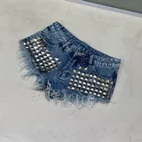 Short de denim azul con efecto deslavado, tiro medio y detalles de tachas piramidales plateadas en los bolsillos delanteros. Los bordes cuentan con terminación desmechada.