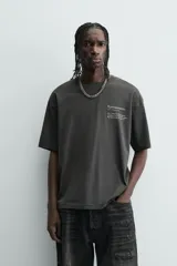 Camiseta de manga corta y cuello redondo, color gris oscuro o negro deslavado, con estampado de texto en blanco en el pecho.