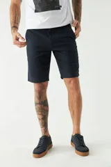 Bermuda tipo china de corte clásico, confeccionada en tejido de algodón con textura. Presenta cierre de cremallera y botón, bolsillos laterales y traseros, y trabillas para cinturón. Incluye un pequeño logo bordado.