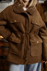 Campera de efecto gamuza color tostado con interior de corderito sintético. Presenta cierre frontal, bolsillos delanteros con solapa, cintura ajustable con cordón y puños con detalle de corderito.