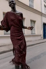 Vestido midi asimétrico de un solo hombro en color bordó, confeccionado en tejido devoré con diseño floral y detalles de terciopelo. Presenta frunces laterales, bajo con flecos largos y aplicación de tachas metálicas. Incluye forro interior y cierre lateral con cremallera oculta.