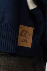 Campera tejida de punto con cierre frontal completo y cuello polo. Presenta un diseño con franja horizontal en color azul y letras en blanco sobre fondo negro, con puños y ruedo acanalados.
