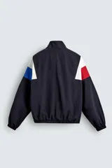 Chaqueta técnica de corte relajado con cuello subido y cierre frontal de cremallera bidireccional. Presenta un diseño color block en tonos azul marino, blanco, rojo y azul eléctrico. Incluye bolsillos frontales de vivo, puños y ruedo elásticos, y forro interior de red.