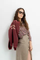 Falda midi de tiro alto confeccionada en tejido tweed con patrón de espiga en tono marrón. Presenta un diseño recto y cierre frontal con botones.