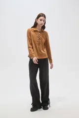 Blusa de gamuza sintética color camel, con cuello camisero y cierre frontal mediante cordones entrelazados. Presenta mangas largas y un corte holgado.