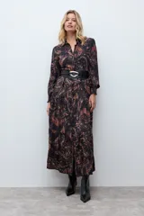 Vestido midi de corte camisero con estampado paisley en tonos oscuros, manga larga con puños ajustados y cierre frontal de botones. Presenta un diseño fluido con falda de volantes en el ruedo.