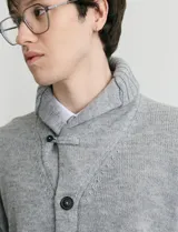 Cardigan de punto color marrón con cuello esmoquin, cierre frontal con botones y presilla superior. Presenta mangas largas con coderas en contraste y bolsillos frontales de ribete.