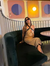 Vestido midi color arena con detalles en cuero negro en el escote, sisas y ruedo. Presenta escote halter cruzado y corte recto.