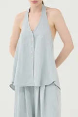 Chaleco halter celeste de viscosa y poliamida, con escote en V profundo, cierre frontal de botones y espalda descubierta.