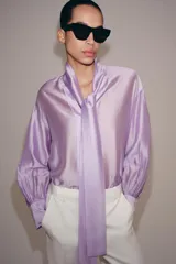 Camisa de ZARA Woman Collection confeccionada en hilatura con mezcla de lyocell, de color blanco marfil. Presenta cuello redondo, escote en V con lazadas en el mismo tejido, manga larga con puño y bajo recto.