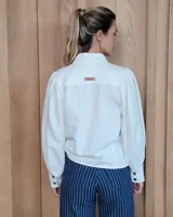 Camisa de color arena con mangas abullonadas, puños anchos con botones y cuello clásico. Presenta un diseño de corte recto con costuras visibles y cierre frontal oculto.