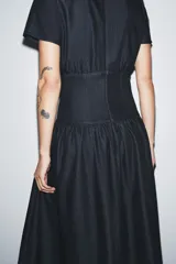 Vestido midi de denim color negro con cuello redondo y manga corta. Presenta un diseño con cintura entallada tipo bustier y falda con corte evasé. Cierre posterior con cremallera.