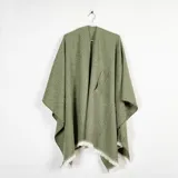 Ruana de tejido de punto en color verde oliva, con diseño abierto y terminaciones con flecos en el ruedo. Presenta un bolsillo frontal aplicado.