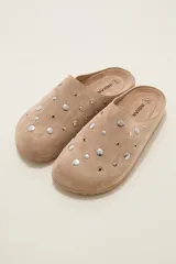 Suecos de gamuza color tostado con diseño de tachas metálicas circulares distribuidas en la parte superior. Presentan una suela plana y cómoda, ideal para uso diario.