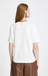 Remera blanca de algodón con cuello redondo y mangas cortas. Presenta un estampado disperso de perros de diferentes razas y colores, junto con un detalle de texto bordado cerca del cuello.