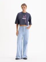 Remera blanca de corte cropped y manga corta, confeccionada en algodón. Presenta una estampa frontal con un conejo con estampado animal print sobre una nube y el texto 'IL BUNNY' en color amarillo.