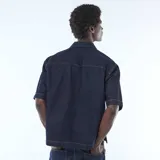 Camisa de jean color azul oscuro con costuras en contraste, cuello clásico, cierre frontal con botones y bolsillo frontal en el pecho.