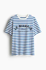 Remera de corte holgado en punto de algodón, con diseño de rayas horizontales azules y blancas, cuello redondo y estampado frontal con la inscripción 'Le Marais Paris'.