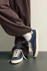 Zapatilla casual de tejido de algodón color beige con detalles en verde y un parche negro en el talón. Cuenta con suela de goma texturizada a contraste.