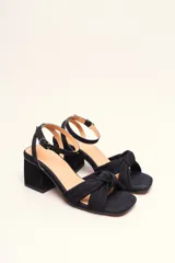 Sandalia de gamuza color beige con taco cuadrado, tira ajustable con hebilla en el tobillo y detalle de nudo en la tira delantera.