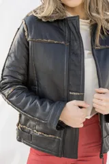 Campera tipo gamulán de cuero genuino color negro, con interior y cuello de piel sintética en tono grisáceo. Presenta cierre frontal, costuras visibles y diseño estructurado.