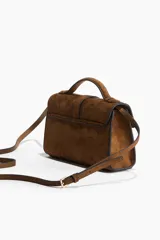 Cartera cruzada de gamuza marrón, con asa superior, correa ajustable y solapa frontal con cierre de mosquetón ovalado metálico.