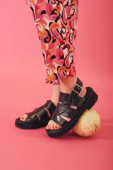 Sandalias de plataforma color negro con diseño de tiras cruzadas y textura tipo cocodrilo. Cuentan con cierre de hebilla metálica en el tobillo y suela plana gruesa.