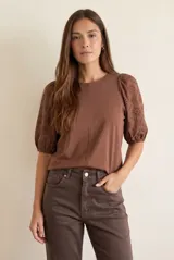 Remera de algodón color marrón, con mangas cortas abullonadas confeccionadas en tela broderie con diseño floral calado y puños elásticos.