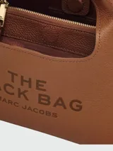 Cartera tipo hobo de cuero negro, con diseño estructurado y asa superior integrada. Presenta el logo de la marca grabado en el frente.