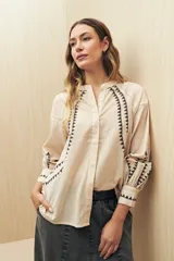 Camisa de lino color beige con bordados geométricos en color negro. Presenta cuello mao, cierre frontal con botones, mangas largas con volumen y puños ajustados.