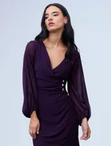 Vestido midi color morado de RM Richards, confeccionado en seda fría. Presenta escote en V cruzado, mangas largas abullonadas de gasa, cintura drapeada y aplique de botones brillantes en el lateral.