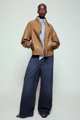 Chaqueta bomber ZW Collection confeccionada en tejido efecto piel de color marrón. Cuenta con cuello subido, manga larga con puño y botón a presión, bolsillos delanteros y bajo recto elástico. Cierre frontal cruzado con botones a presión.