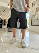 Bermuda baggy de jean negro, con costuras visibles en blanco y diseño holgado.