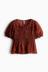 Blusa marrón de lyocell con escote redondo, mangas cortas abullonadas y cuerpo fruncido con detalle de tiras decorativas.