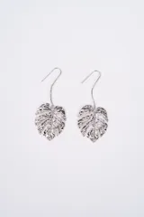 Aros colgantes plateados con diseño de hoja de monstera texturizada y gancho tipo anzuelo.