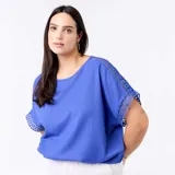 Camiseta azul con cuello redondo, mangas cortas holgadas y detalles de encaje y macramé en las costuras de las mangas.
