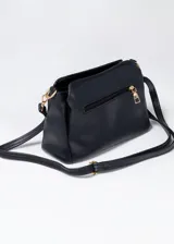 Cartera negra de cuero sintético con textura tipo piel de cocodrilo. Tiene correa larga regulable, cinco compartimentos con cierre y herrajes dorados.