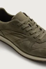 Zapatilla deportiva de estilo casual, confeccionada en una combinación de piezas de cuero con acabado serraje. Presenta horma redonda, cierre con cordones y suela dentada en contraste.