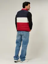 Chaleco acolchado de diseño color block con franjas horizontales en azul marino, blanco y rojo. Presenta cuello alto, cierre frontal de cremallera y dos bolsillos laterales con cierre. Incluye logo de la marca bordado en el pecho.