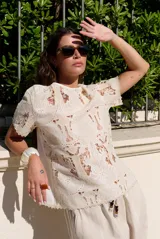 Blusa de encaje con diseño floral y geométrico translúcido, de manga corta y cuello redondo.