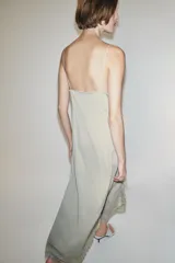 Vestido largo lencero de tejido fluido en color gris verdoso, con escote en V, tirantes finos y detalles de encaje a tono en el bajo y los laterales, además de una abertura frontal.