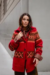 Saco tejido a mano con diseño jacquard en tonos rojo, naranja y marrón. Presenta cuello tipo polo, cierre frontal con botones grandes, mangas largas y tajos laterales en el ruedo.