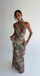 Vestido largo estampado con diseño tropical, escote halter profundo y detalle de argolla metálica en el centro del busto. Presenta aberturas laterales en la cintura y falda con caída fluida.