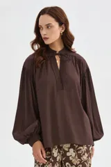 Blusa de lyocell color marrón, con diseño holgado, escote en V con cordón para atar y mangas largas abullonadas con puños ajustados.