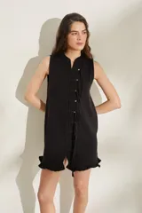 Vestido corto de punto sin mangas, color negro, con cuello redondo y cierre frontal decorado con botones y tiras colgantes. Presenta terminaciones con volados en el ruedo.
