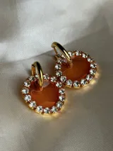 Aros colgantes dorados con dije circular de resina color turquesa, bordeado con strass. El arito es de acero quirúrgico.