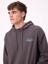 Canguro gris claro con capucha y estampado trasero en azul. El estampado incluye el texto "Spirit League Rusty Team" y una ilustración de una camioneta con animales y tablas de surf.