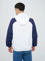 Campera deportiva Umbro del Club Nacional de Football, modelo Venti, para hombre. Diseño en color blanco con mangas azules y detalles de líneas rojas. Cuenta con capucha con cordón ajustable, cierre frontal y bolsillos. Presenta el logo de Umbro y el escudo del club bordados en el pecho.